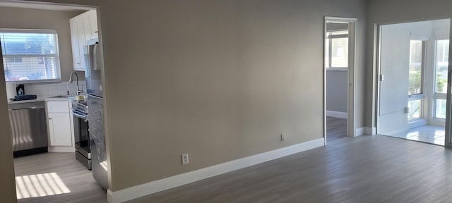 interior space featuring light wood-style floors, baseboards, white cabinets, a sink, and stainless steel appliances