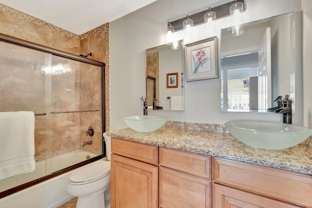 full bath with a sink, double vanity, toilet, and enclosed tub / shower combo