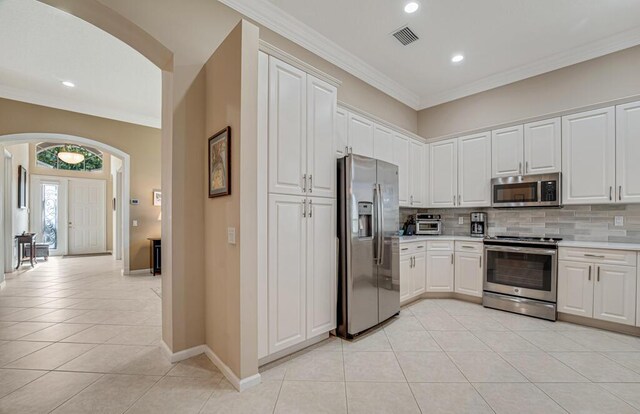 kitchen with stainless steel appliances, arched walkways, light tile patterned floors, light countertops, and backsplash