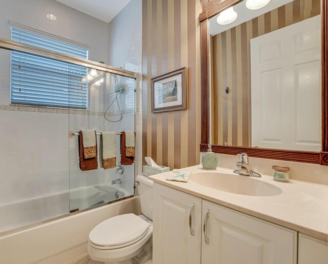 full bath with wallpapered walls, toilet, shower / bath combination with glass door, and vanity