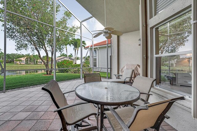 view of patio / terrace featuring a water view, ceiling fan, outdoor dining space, and a lanai