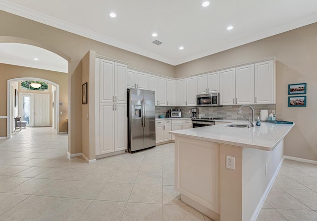 kitchen with appliances with stainless steel finishes, arched walkways, a peninsula, light tile patterned flooring, and recessed lighting