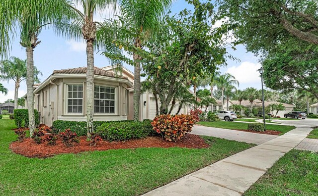 view of side of property with a yard, a tile roof, driveway, and stucco siding