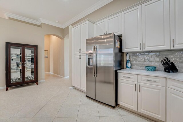 kitchen with stainless steel fridge, arched walkways, ornamental molding, light tile patterned floors, and backsplash
