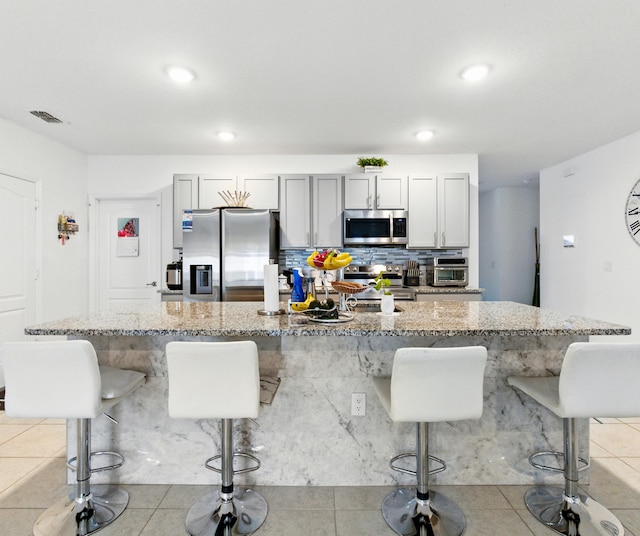 3020 SW Ann Arbor Rd, Port Saint Lucie, FL 34953 - kitchen featuring appliances with stainless steel finishes, a kitchen breakfast bar, light stone counters, light tile patterned flooring, and a kitchen island with sink