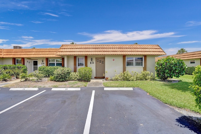 ranch-style house featuring a front yard, stucco siding, a tiled roof, and uncovered parking