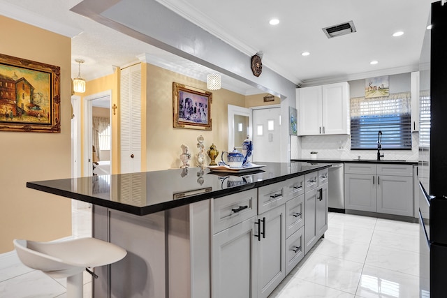 kitchen featuring visible vents, a sink, a kitchen breakfast bar, backsplash, and dark countertops