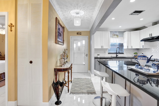 kitchen with a sink, a breakfast bar, visible vents, under cabinet range hood, and crown molding