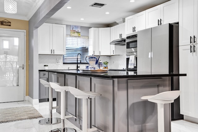 kitchen featuring a sink, stainless steel appliances, ornamental molding, a breakfast bar area, and visible vents