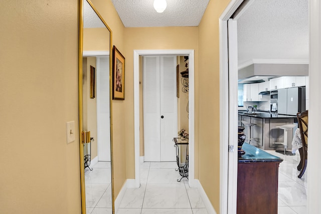 hall featuring a textured ceiling, baseboards, and marble finish floor
