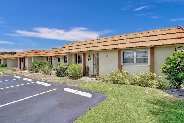 ranch-style house featuring a tiled roof, stucco siding, a front yard, and uncovered parking