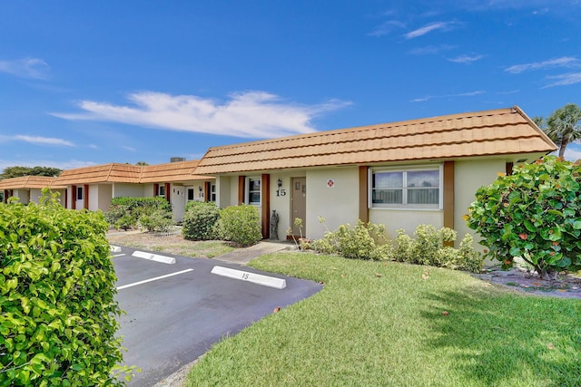 ranch-style house with stucco siding, a tiled roof, a front lawn, and uncovered parking