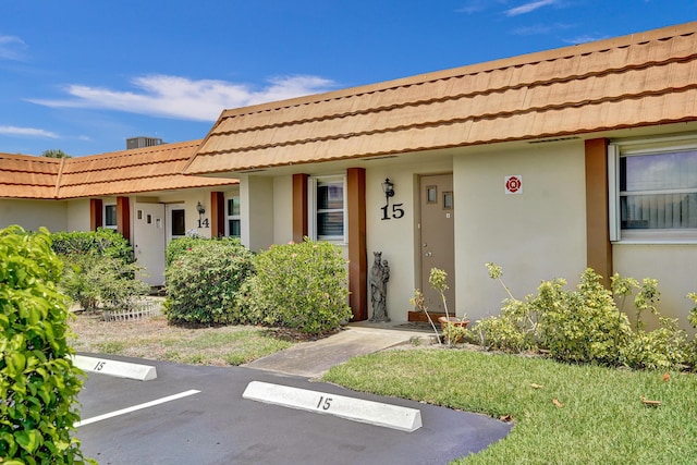 entrance to property featuring a tiled roof, stucco siding, and uncovered parking