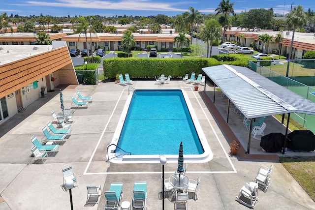 community pool with a patio area, fence, and a residential view