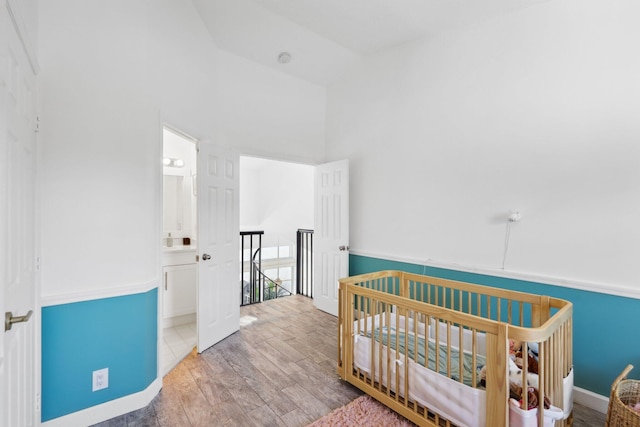 bedroom featuring baseboards, a crib, wood finished floors, and high vaulted ceiling