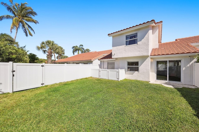 back of property featuring a tiled roof, a lawn, a gate, and a fenced backyard
