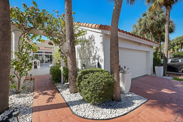 view of side of home featuring an attached garage, stucco siding, driveway, and a tile roof