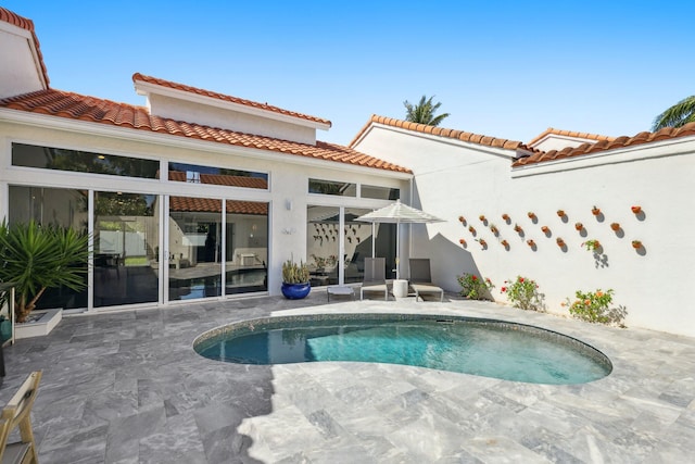 rear view of property featuring a patio, stucco siding, a tile roof, and an outdoor pool