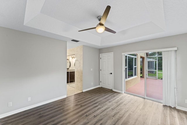 spare room featuring a raised ceiling, wood finished floors, ceiling fan, baseboards, and a textured ceiling