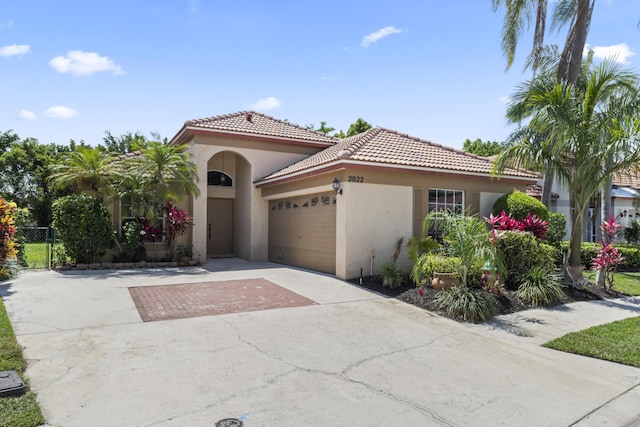 mediterranean / spanish home with stucco siding, a garage, a tile roof, concrete driveway, and fence