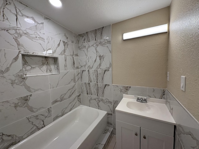 bathroom with tile walls, shower / bathtub combination, a textured ceiling, vanity, and a textured wall