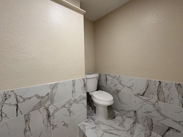 half bathroom with toilet, tile walls, and marble finish floor