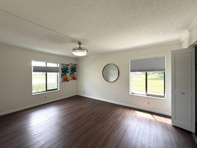 spare room featuring dark wood finished floors, a textured ceiling, crown molding, and baseboards