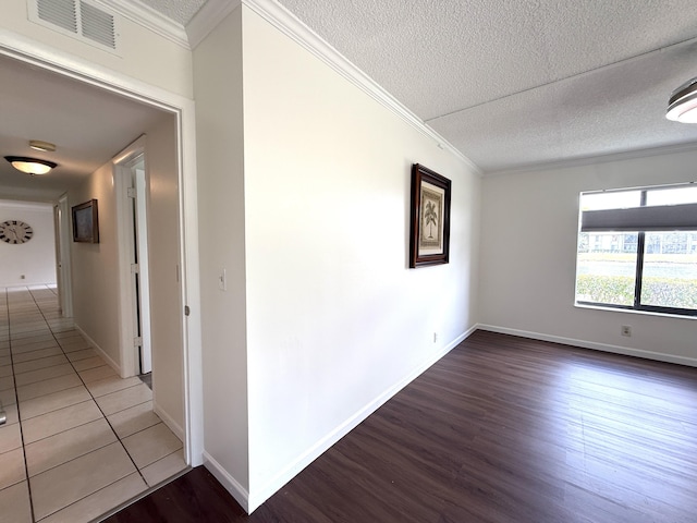 hallway with wood finished floors, a textured ceiling, ornamental molding, and baseboards