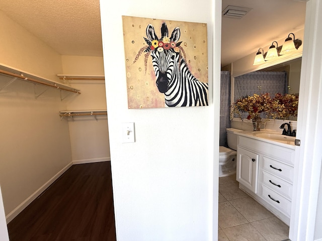 full bath featuring toilet, vanity, a spacious closet, and baseboards