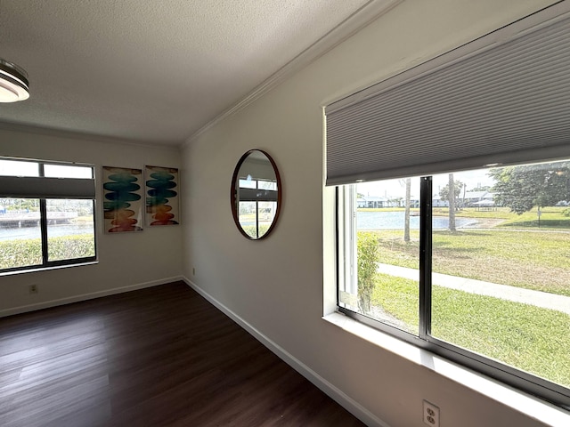 empty room with crown molding, healthy amount of natural light, dark wood finished floors, baseboards, and a textured ceiling