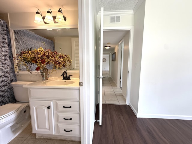 bathroom with toilet, vanity, wood finished floors, and crown molding