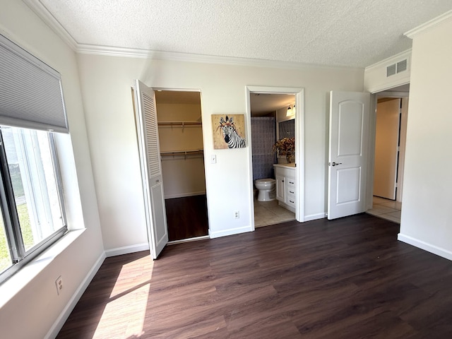 unfurnished bedroom with a textured ceiling, crown molding, dark wood finished floors, baseboards, and a walk in closet