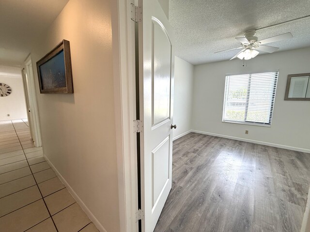corridor featuring baseboards, wood finished floors, and a textured ceiling