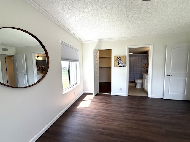 unfurnished bedroom featuring a textured ceiling, wood finished floors, ornamental molding, baseboards, and a spacious closet