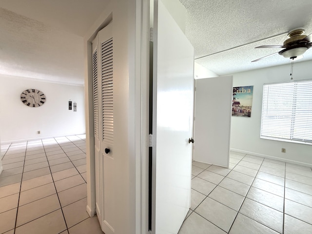 hall with light tile patterned floors, a textured ceiling, and baseboards