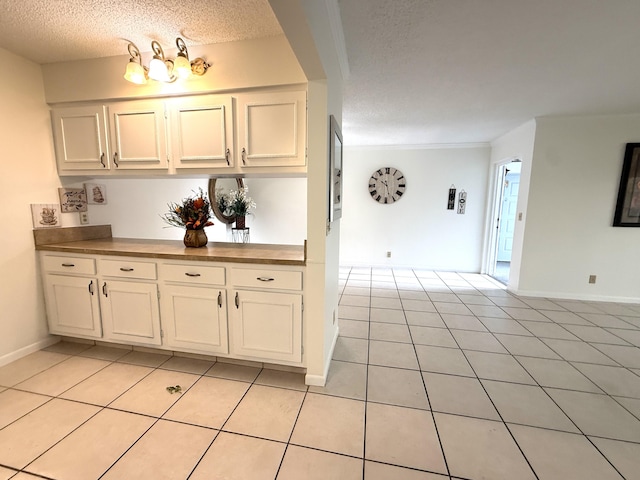kitchen with a textured ceiling, light tile patterned floors, baseboards, and white cabinetry