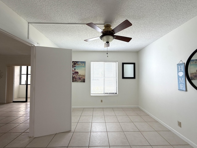 empty room featuring ceiling fan, light tile patterned floors, a textured ceiling, and baseboards