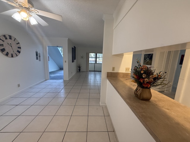 hall featuring light tile patterned floors, a textured ceiling, and baseboards