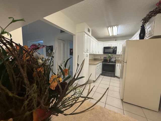 kitchen featuring freestanding refrigerator, electric stove, black microwave, light tile patterned flooring, and a textured ceiling