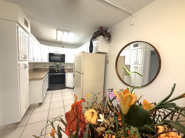 kitchen with electric range, black microwave, freestanding refrigerator, light tile patterned flooring, and white cabinetry