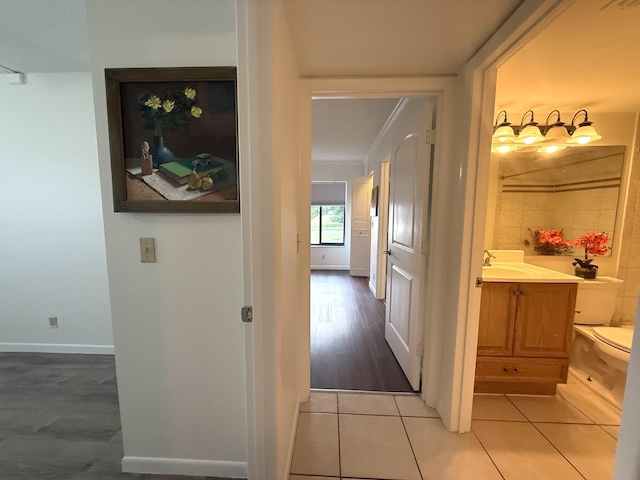 corridor featuring light tile patterned flooring, ornamental molding, baseboards, and a sink