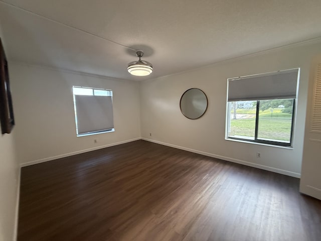 empty room featuring ornamental molding, healthy amount of natural light, dark wood-style flooring, and baseboards