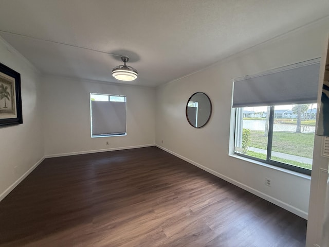 empty room with dark wood-style floors, baseboards, and a water view