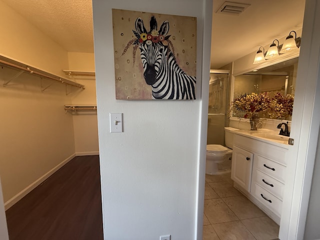 full bath with a stall shower, vanity, a walk in closet, toilet, and baseboards