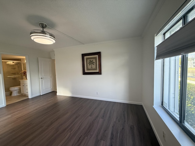 unfurnished bedroom featuring dark wood-style floors, baseboards, a textured ceiling, connected bathroom, and ornamental molding