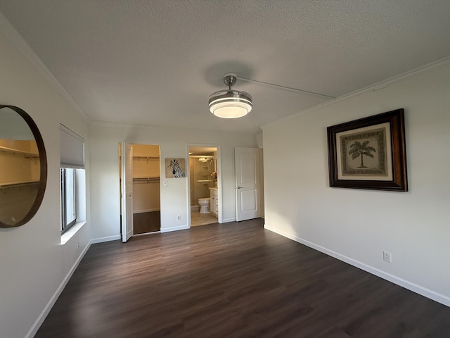 unfurnished bedroom featuring dark wood-type flooring, baseboards, a textured ceiling, a walk in closet, and a closet