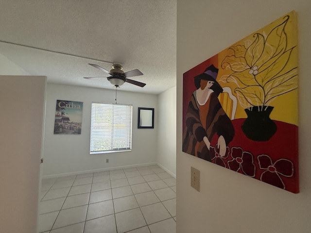 empty room featuring a ceiling fan, a textured ceiling, baseboards, and light tile patterned flooring