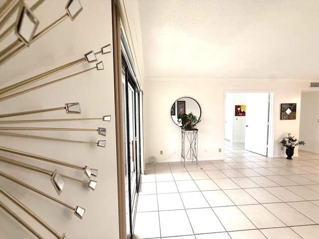 hall with light tile patterned flooring, ornamental molding, a textured ceiling, and baseboards