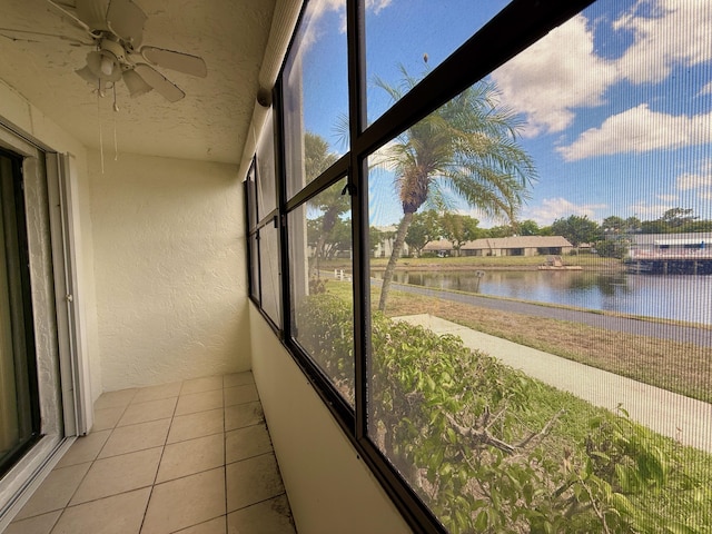 unfurnished sunroom featuring a textured wall, a water view, ceiling fan, tile patterned floors, and a textured ceiling