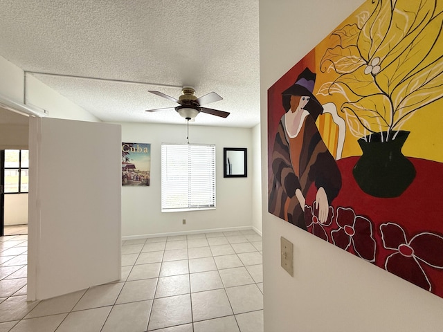 tiled empty room with a ceiling fan, plenty of natural light, a textured ceiling, and baseboards